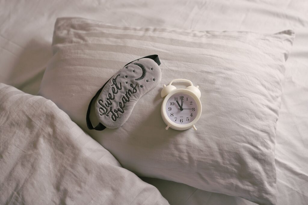 An eyemask and alarm clock on a pillow to symolize our Improve your Snooze workshop